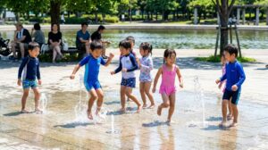 夏の陽射しの下、舎人公園の水遊びエリア（じゃぶじゃぶ池）で元気いっぱいに水しぶきをあげて遊ぶ日本人 の子供たち。家族連れに大人気のスポット。