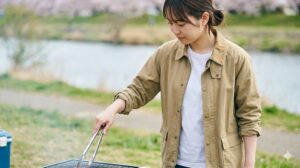 難燃加工が施されたコットン素材のジャケットを着用し、安全に配慮しながらバーベキューコンロで食材を調理する女子大学生の様子。火の粉への対策が万全であることを示している。