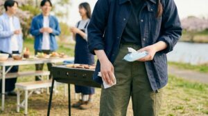 バーベキュー会場で、濃いネイビーブルーのコットンジャケットを着用した女子大学生。汚れても目立ちにくく、丈夫な素材で、汚れを気にするストレスを軽減している。